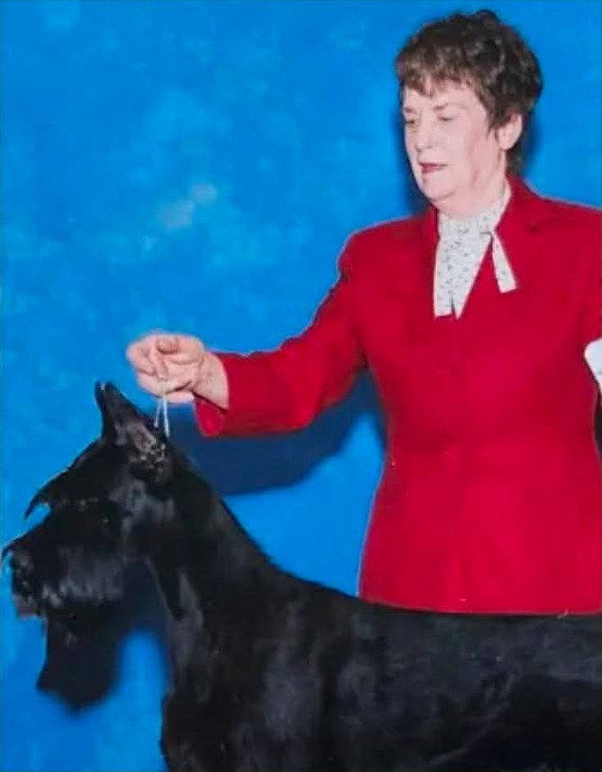 Doloris H. Wells in a red jacket, showing one of her black Giant Schnauzers
